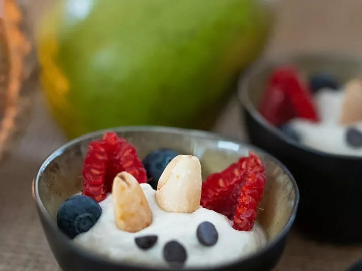 Crème de cajou et poires dans un ramequin noir, avec framboises, myrtilles et amandes, une poire verte en arrière-plan