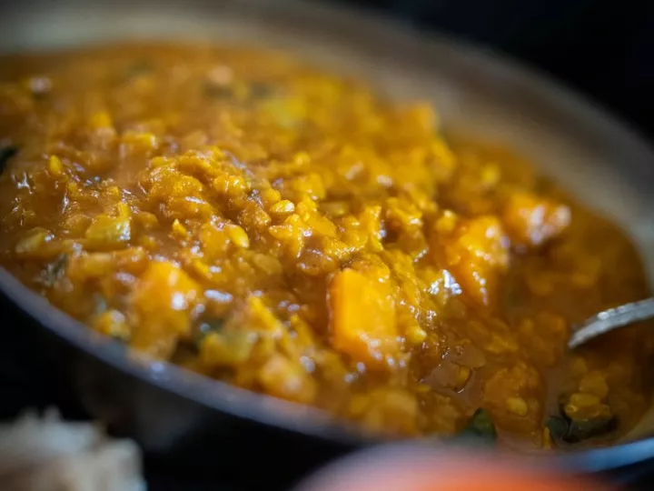 Gros plan sur un dahl de lentilles rouges avec des morceaux de patate douce, bougies floues au premier plan