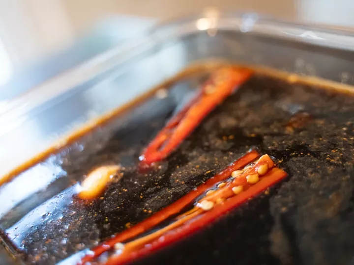 Marinade de sauce soja et de mirin avec deux moitiés de piment rouge et une gousse d'ail dans un plat en verre