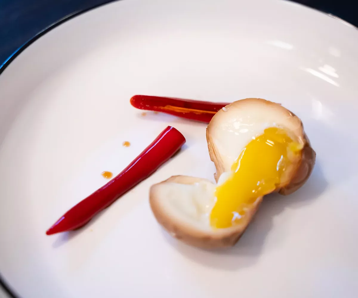 Œuf mariné coupé en deux avec un jaune coulant, à côté de deux morceaux de piment rouge sur une assiette blanche