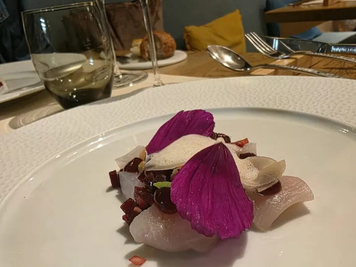 Flétan mariné et fumé, betterave, noisettes et pétales violets sur une assiette blanche, chez Luma