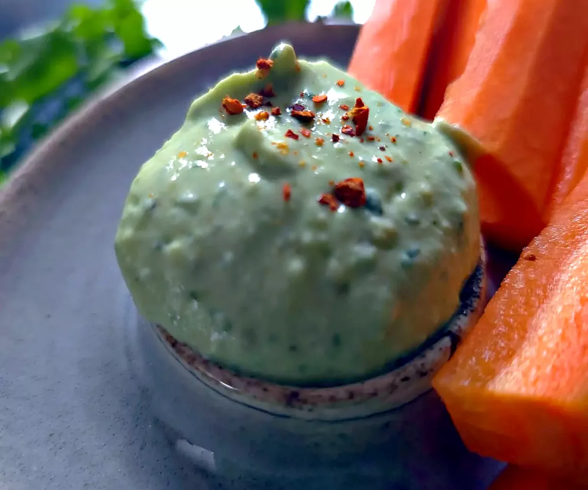 Dôme de sauce verte à l'avocat, au yaourt grec et à la coriandre, parsemé de flocons de piment, avec des bâtonnets de carotte
