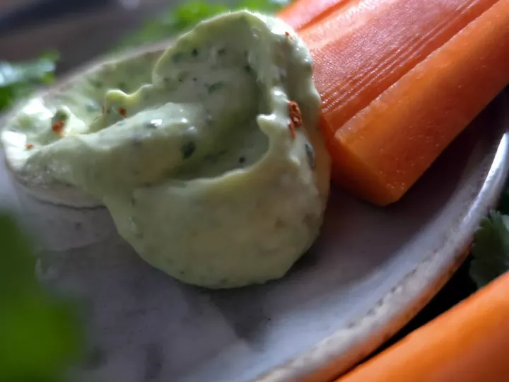 Sauce verte à l'avocat et à la coriandre bien onctueuse dans une assiette en grès, à côté de carottes