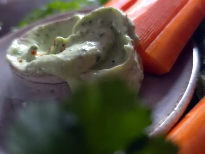 Tourbillon de sauce verte à l'avocat et à la coriandre dans une assiette en grès, avec des carottes et de la coriandre